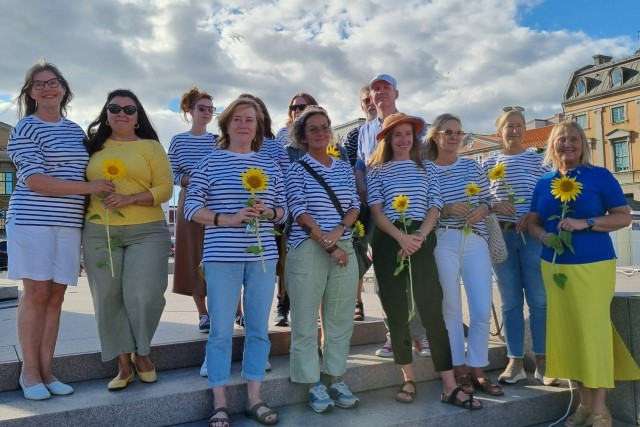 Gruppbild på personer från Litorina folkhögskola. De är alla iklädda gult, vitt och blått och håller i vars en solros.