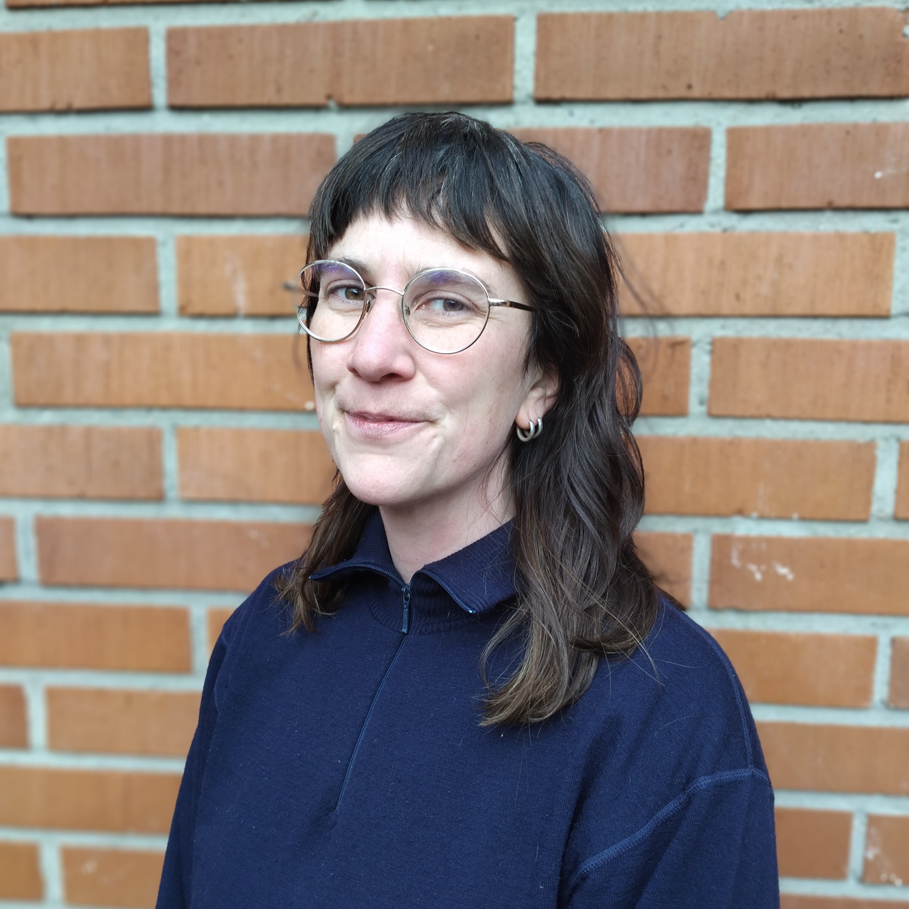 Foto på Linnea Isberg framför röd tegelvägg.