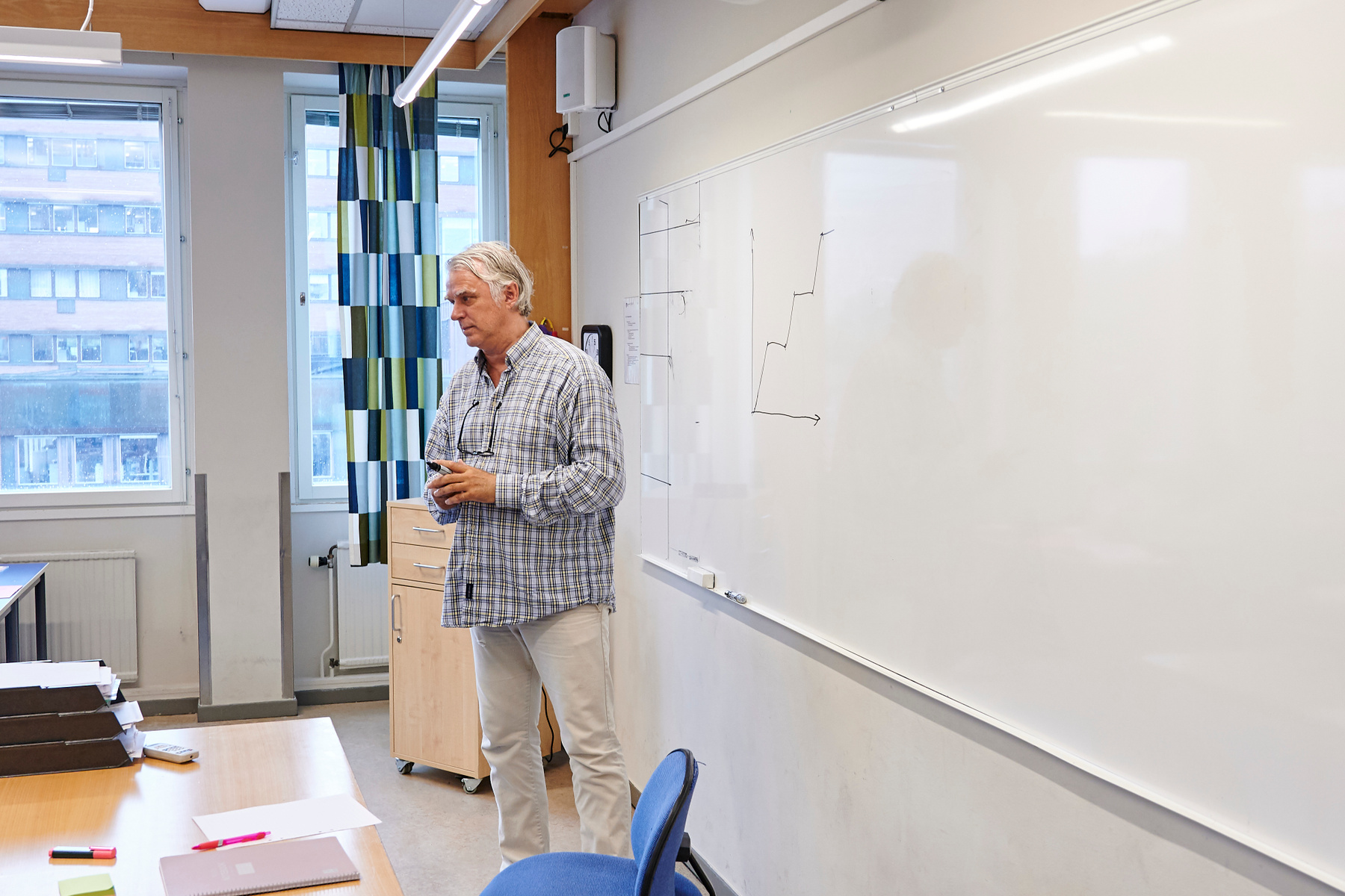 En lärare står i ett klassrum framför en whiteboardtavla och undervisar.