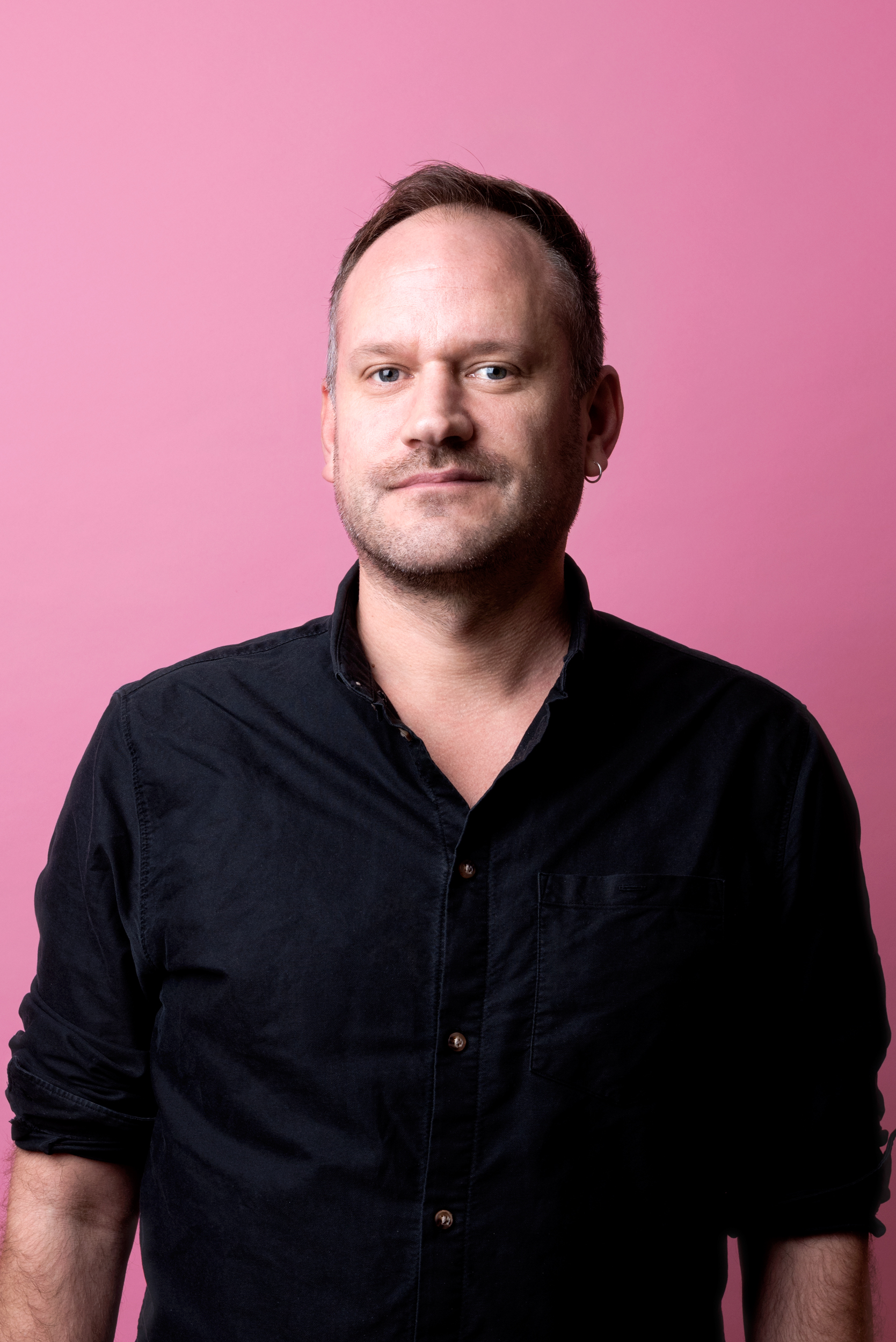 Joel tittar rakt in i kameran och bär en svart skjorta. Han har kort brunt hår med lite gråa toner.