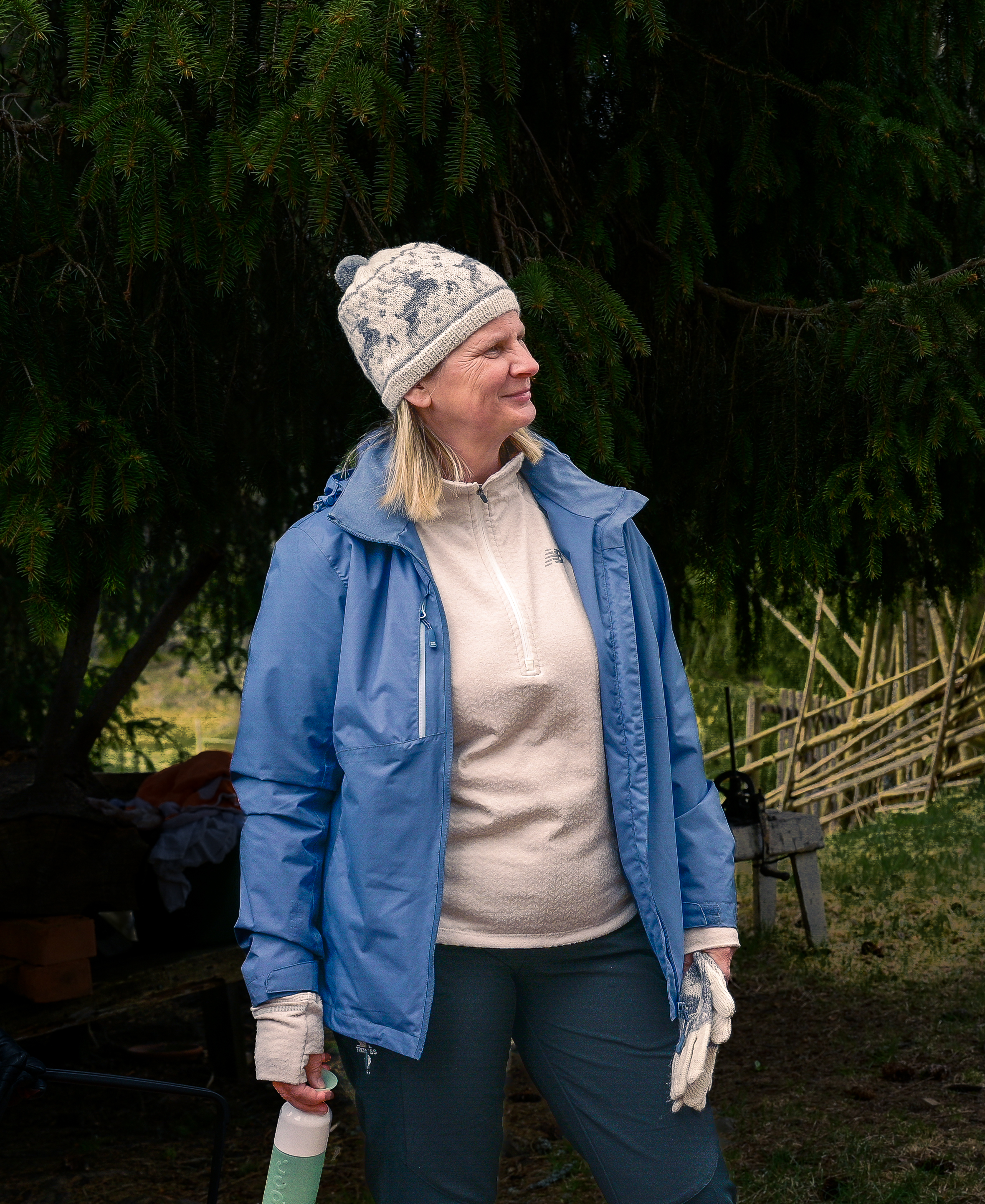 Ingela Johansson står i naturen iklädd en stickad mössa och en blå jacka, hon tittar lite åt sidan och ser glad ut.