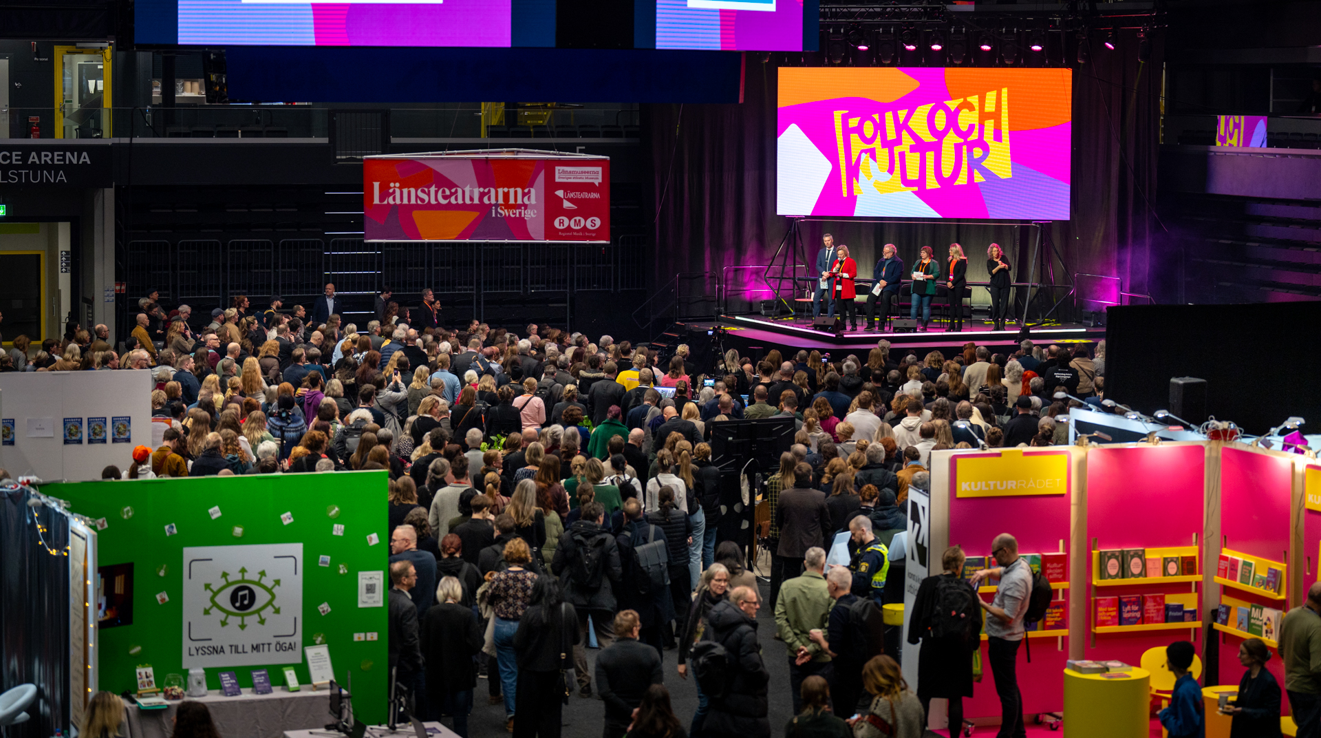 Publik framför en scen sett från ovan, bakom scenen syns en skärm med Folk och Kulturs logotyp.