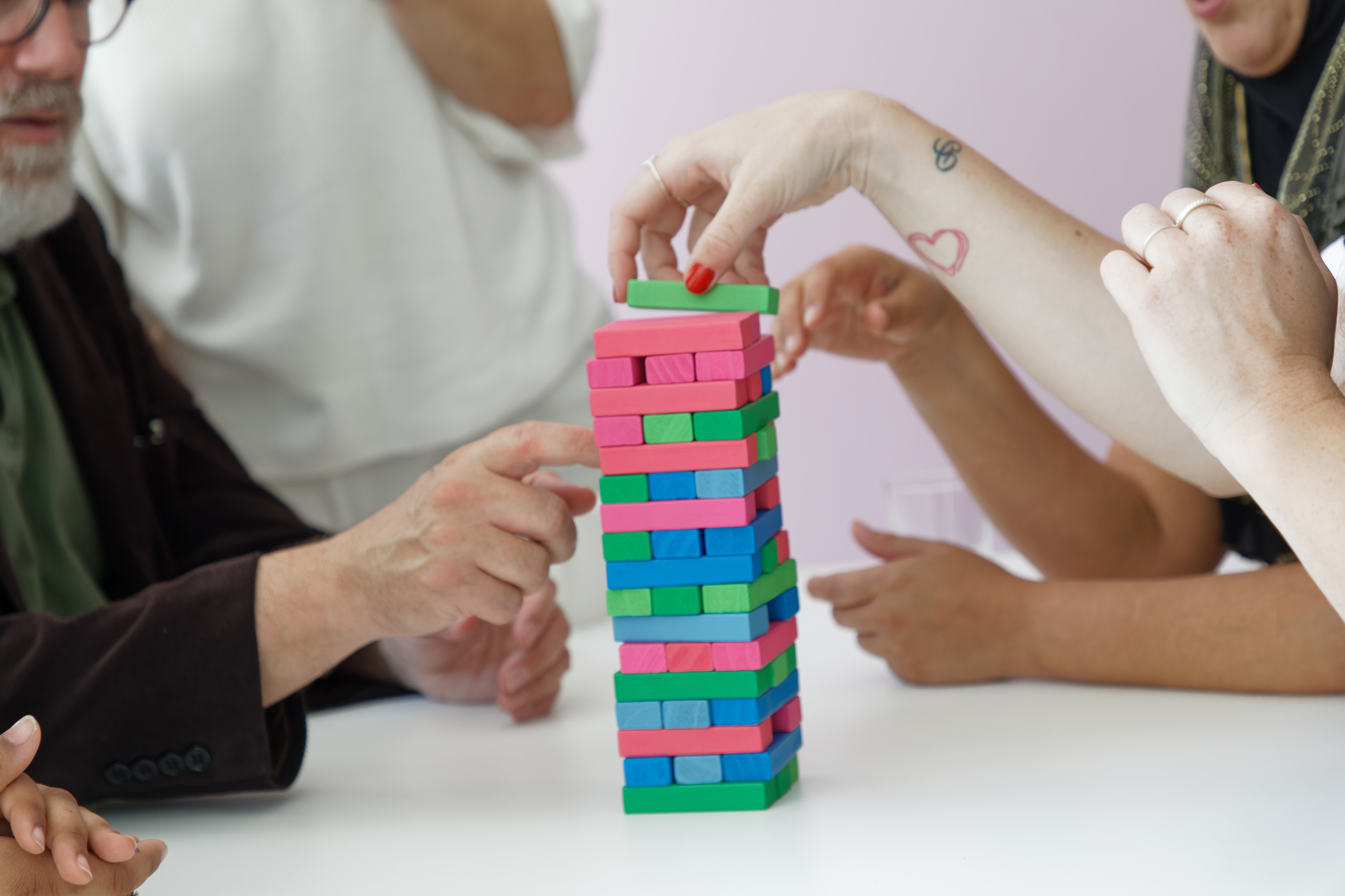 En grupp människor bygger tillsammans ett torn av olikfärgade leksaksklossar.