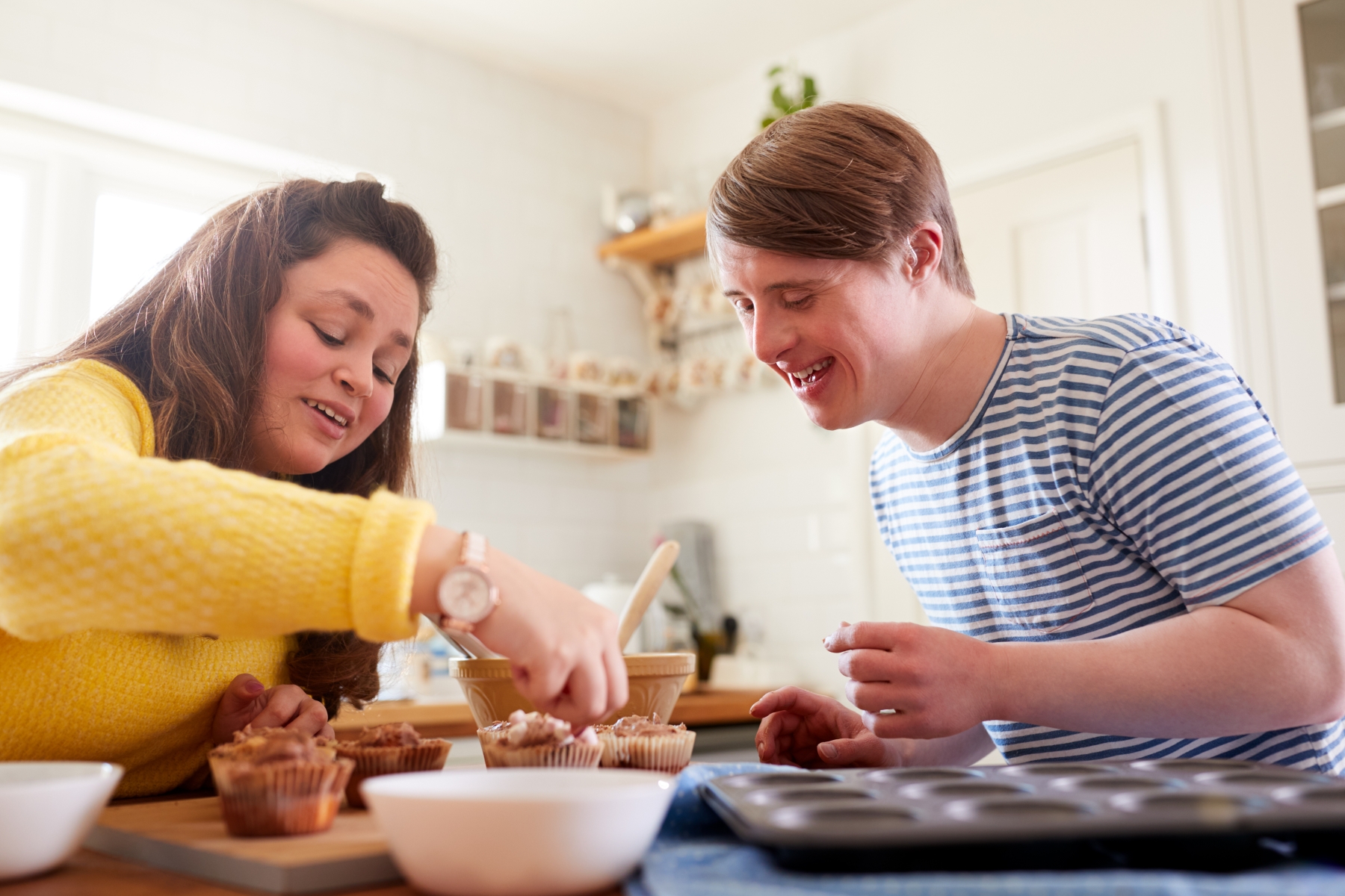 Två personer bakar muffins, en av dem har downs syndrom. De ser båda glada ut.