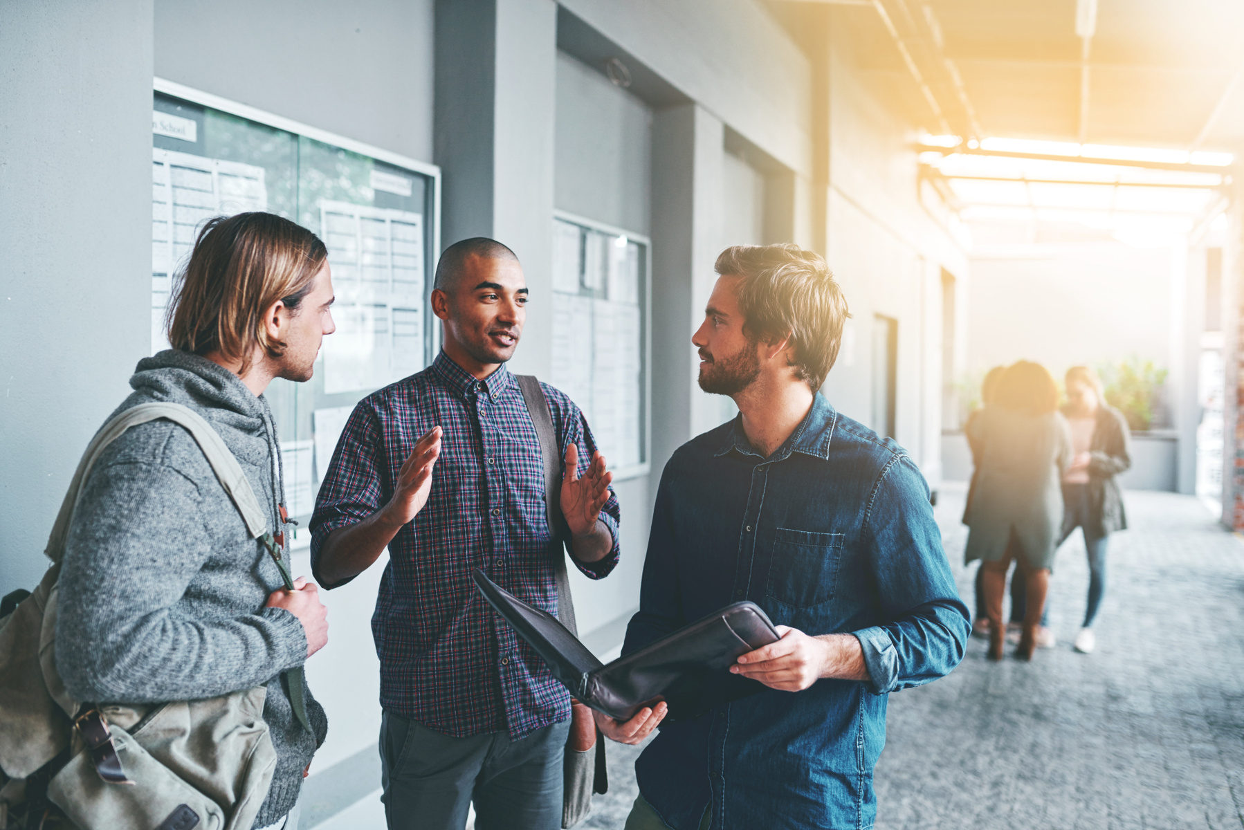 Tre män står och diskuterar, en av dem håller upp en pärm och visar något för de andra.